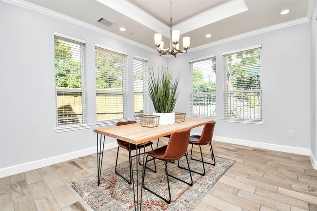 Bright dining room with large windows, modern chandelier, and a stylish wooden table with seating for six. Light wood flooring complements the neutral wall tones, creating an inviting and airy space. | Image 12