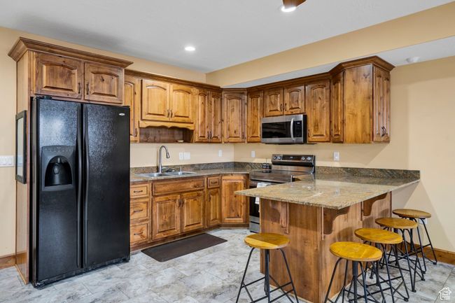Kitchen with a peninsula, appliances with stainless steel finishes, a sink, a breakfast bar area, and brown cabinetry | Image 33