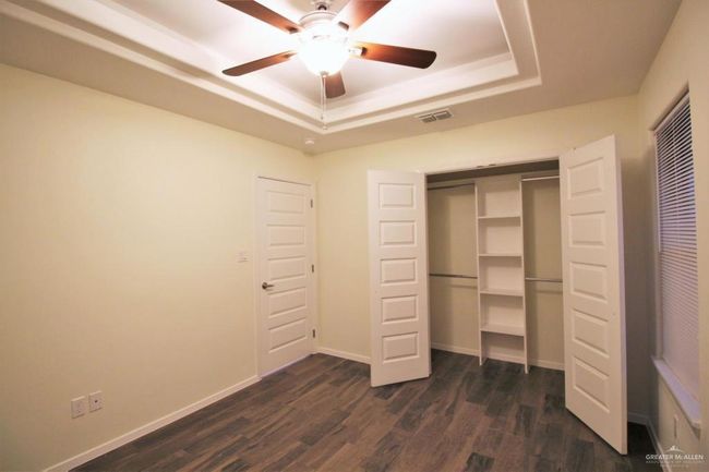 Unfurnished bedroom featuring a raised ceiling, dark wood-type flooring, a closet, and ceiling fan | Image 5