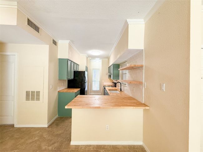Kitchen with green cabinetry, open shelves, crown molding, butcher block countertops, and freestanding refrigerator | Image 9