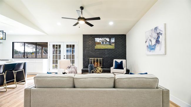 Living area with light wood finished floors, french doors, ceiling fan, and a fireplace | Image 5