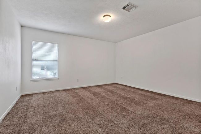 This photo showcases a spacious room with neutral color walls and carpet flooring. It features a large window that allows natural light to fill the space, and a ceiling light fixture. | Image 26