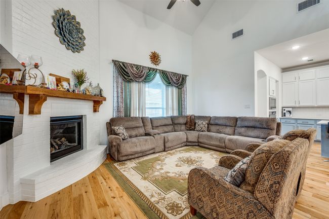 Living area with high vaulted ceiling, light wood-type flooring, ceiling fan, a fireplace, and arched walkways | Image 5