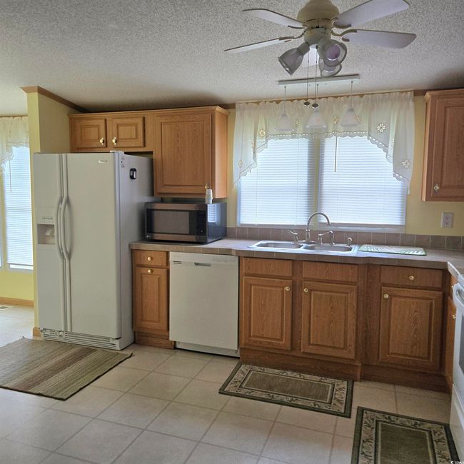 Kitchen with a textured ceiling, white appliances, a ceiling fan, light tile patterned floors, and brown cabinets | Image 15