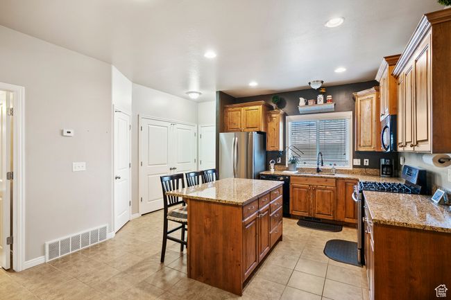 Kitchen featuring black appliances, a breakfast bar, a kitchen island, light stone countertops, and recessed lighting | Image 8