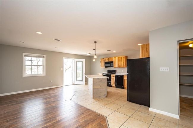 Kitchen featuring black appliances, a kitchen island, light wood finished floors, baseboards, and light countertops | Image 7