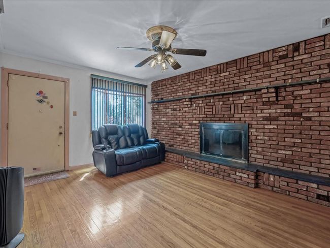 Living area featuring hardwood / wood-style floors, ceiling fan, a fireplace, and brick wall | Image 5
