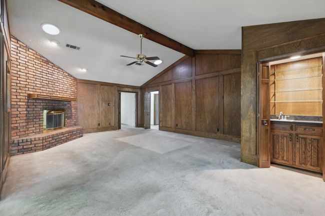 Unfurnished living room featuring a ceiling fan, lofted ceiling with beams, wooden walls, a fireplace, and visible vents | Image 19