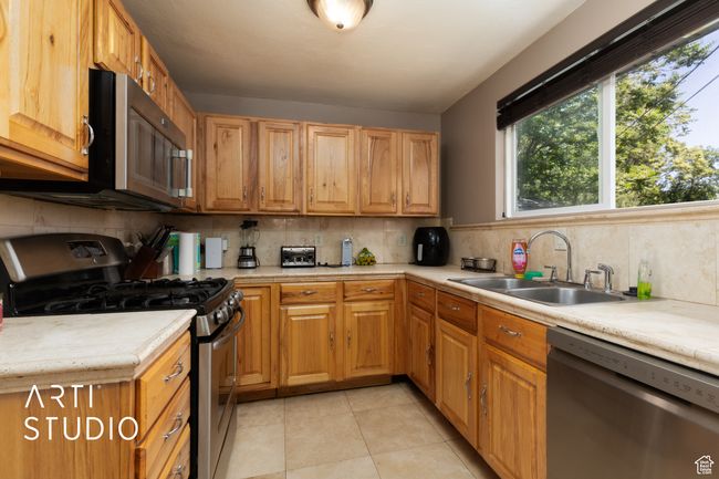 Kitchen with appliances with stainless steel finishes, a sink, light countertops, tasteful backsplash, and light tile patterned flooring | Image 42