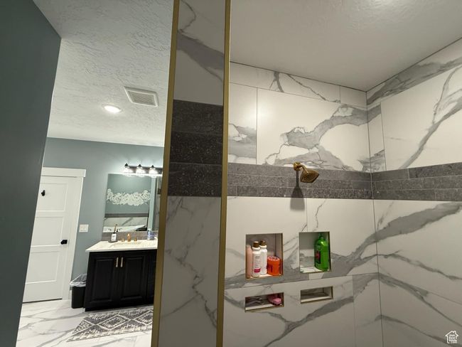 Bathroom with a textured ceiling, visible vents, marble finish floor, a marble finish shower, and vanity | Image 36