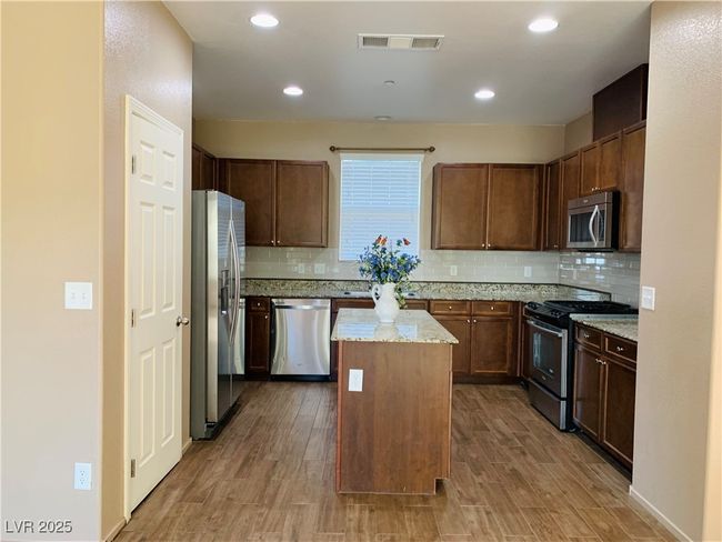 Kitchen featuring visible vents, a center island, light stone counters, decorative backsplash, and appliances with stainless steel finishes | Image 6