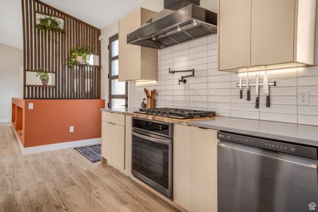 Kitchen with tasteful backsplash, wall chimney exhaust hood, stainless steel appliances, light wood-style flooring, and cream cabinets | Image 5