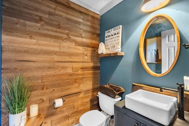 This cozy bathroom features a rustic wood accent wall and a modern sink with a sleek black cabinet. The space is complemented by a round mirror, ambient lighting, and decorative items, creating a warm and inviting atmosphere. | Image 24
