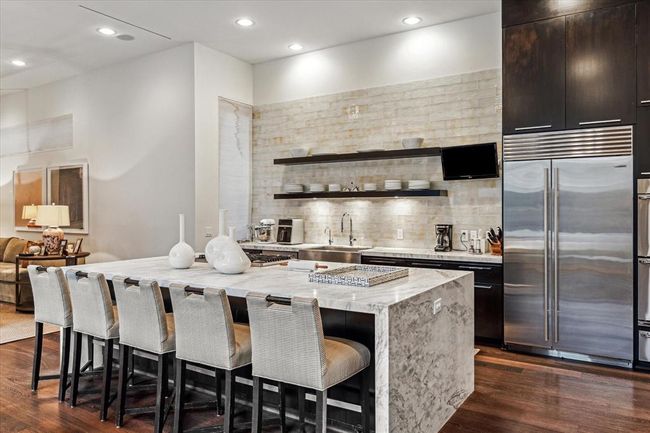 What a fabulously organized and appointed KITCHEN (18 X 11) with its oversized Center Island - allowing for five breakfast bar seats - impressive is its dramatic marble slab counter and side panels. Notice the stainless two compartment sink with decorative fixture/purified water dispenser, marble slab counter/onyx subway tile backsplash, black shelving with under shelf lighting, stainless Dacor 5 gas cooktop, stainless Asko dishwasher, SubZero side by side refrigerator, dual Dacor ovens/warming drawer. | Image 10