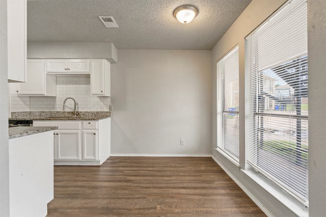 Kitchen with a sink, light stone countertops, tasteful backsplash, dark wood-type flooring, and white cabinets | Image 7