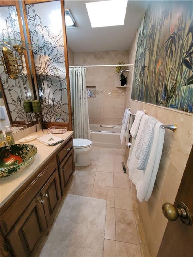 Bathroom featuring tile patterned floors, toilet, a skylight, shower / bath combo with shower curtain, and visible vents | Image 50