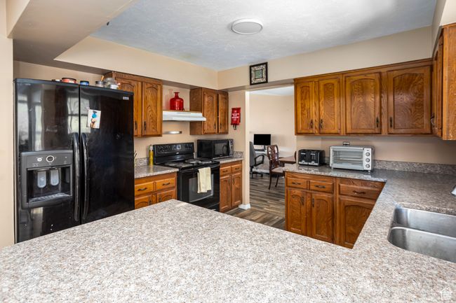 Kitchen featuring a toaster, under cabinet range hood, brown cabinets, black appliances, and a sink | Image 7