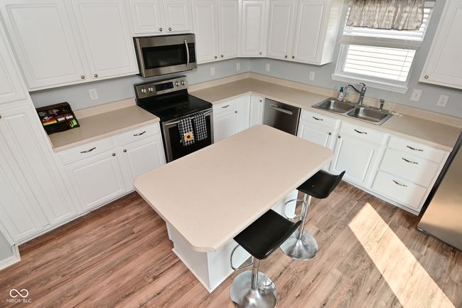 kitchen featuring stainless steel appliances, a sink, white cabinets, a kitchen breakfast bar, and light wood finished floors | Image 23
