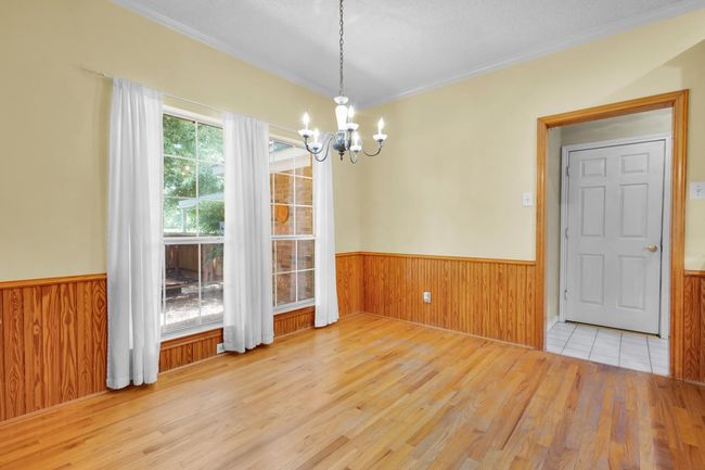 Unfurnished dining area with a chandelier, wood finished floors, a wainscoted wall, wooden walls, and ornamental molding | Image 5