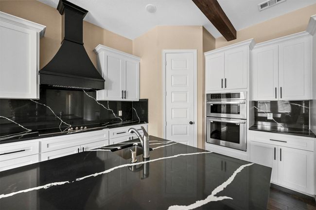Kitchen with double oven, dark countertops, white cabinetry, and custom exhaust hood | Image 29