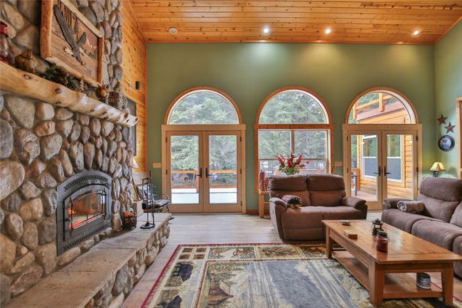 Living room with a stone fireplace, french doors, plenty of natural light, and wood ceiling | Image 11