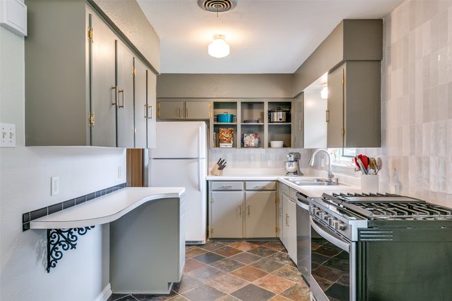 Kitchen with freestanding refrigerator, stainless steel gas range oven, open shelves, and light countertops | Image 9