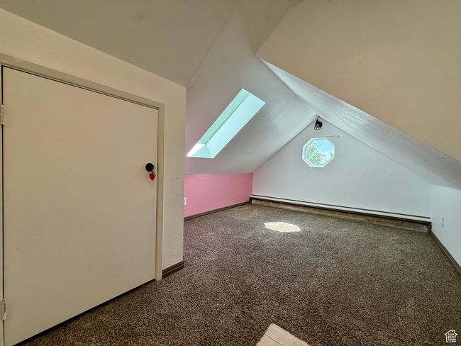 Bonus room featuring a skylight, carpet, vaulted ceiling, a baseboard radiator, and baseboards | Image 25