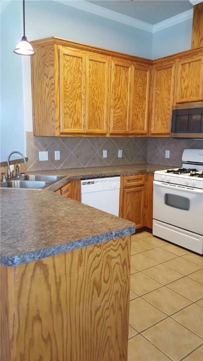 Kitchen featuring white appliances, a peninsula, tasteful backsplash, ornamental molding, and light tile patterned floors | Image 11