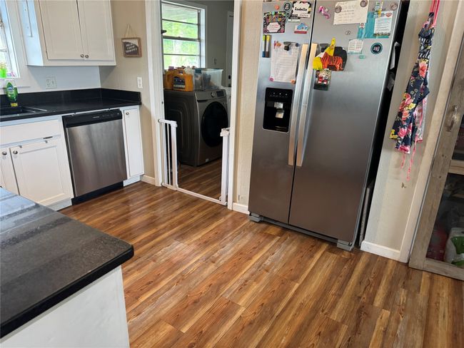 Kitchen with stainless steel appliances, light wood-style flooring, washing machine and clothes dryer, white cabinets, and dark countertops | Image 4