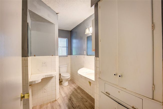 Bathroom with tile walls, toilet, wood finished floors, a textured ceiling, and a wainscoted wall | Image 27
