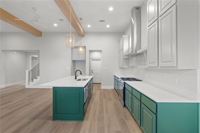 Kitchen with wall chimney range hood, white cabinets, stainless steel range with gas stovetop, light hardwood / wood-style floors, and sink | Image 9