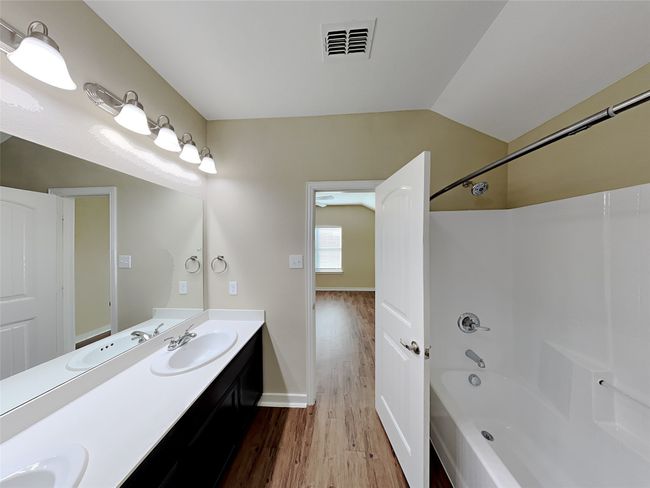 Full bathroom featuring wood finished floors, double vanity, washtub / shower combination, and vaulted ceiling | Image 15