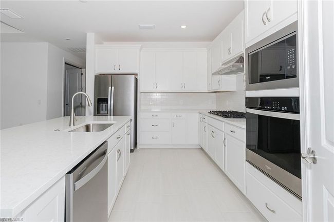 Kitchen featuring stainless steel appliances, under cabinet range hood, light countertops, white cabinets, and tasteful backsplash | Image 15