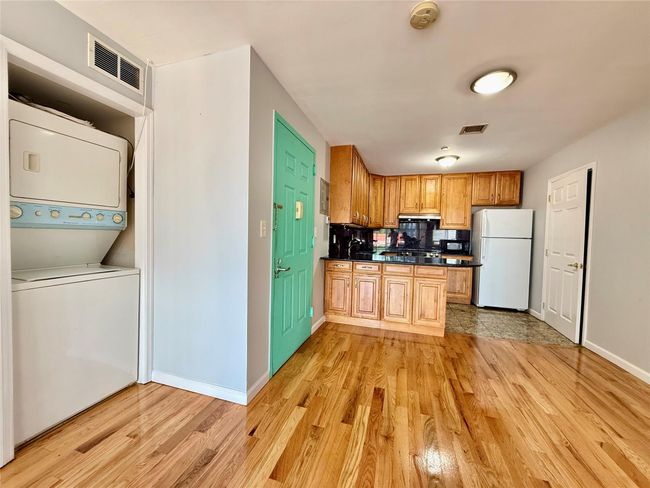 Kitchen featuring freestanding refrigerator, stacked washing machine and dryer, dark countertops, and light wood-style floors | Image 12