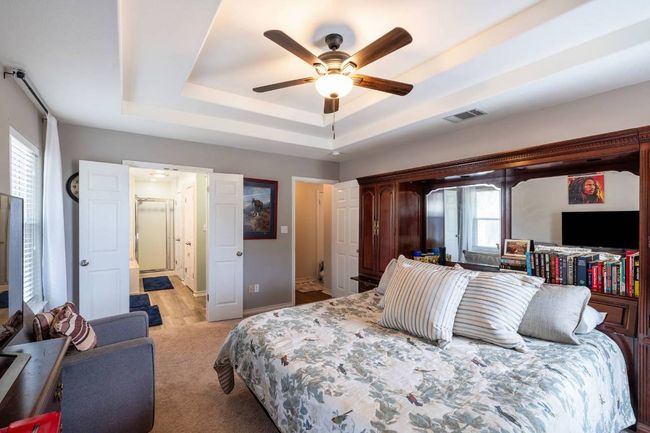Bedroom with ceiling fan, light carpet, visible vents, and a raised ceiling | Image 23