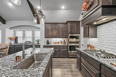 Kitchen featuring custom exhaust hood, tasteful backsplash, appliances with stainless steel finishes, light hardwood / wood-style floors, and sink | Image 3