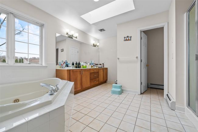 Full bath featuring visible vents, a skylight, a baseboard heating unit, and a tub with jets | Image 24