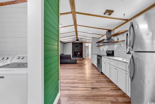Kitchen with stainless steel range with electric stovetop, open shelves, wall chimney exhaust hood, a ceiling fan, and a brick fireplace | Image 7