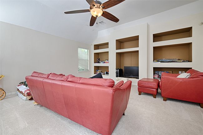 Carpeted living area featuring visible vents, baseboards, ceiling fan, vaulted ceiling, and built in shelves | Image 12
