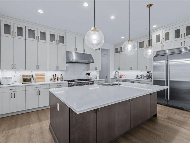 Kitchen with light countertops, under cabinet range hood, a sink, an island with sink, and appliances with stainless steel finishes | Image 6