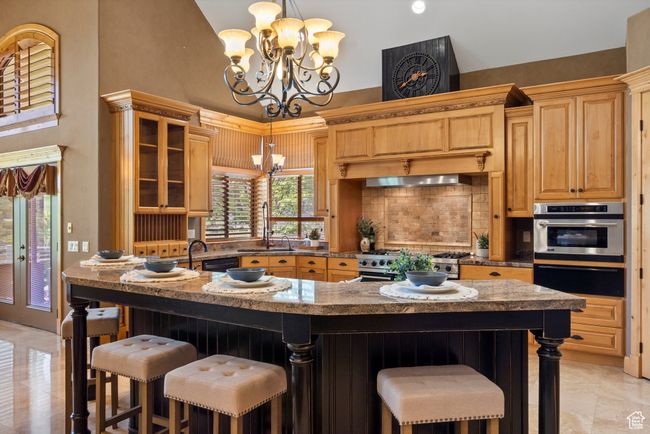Kitchen featuring a chandelier, a warming drawer, appliances with stainless steel finishes, a high ceiling, and a breakfast bar area | Image 31