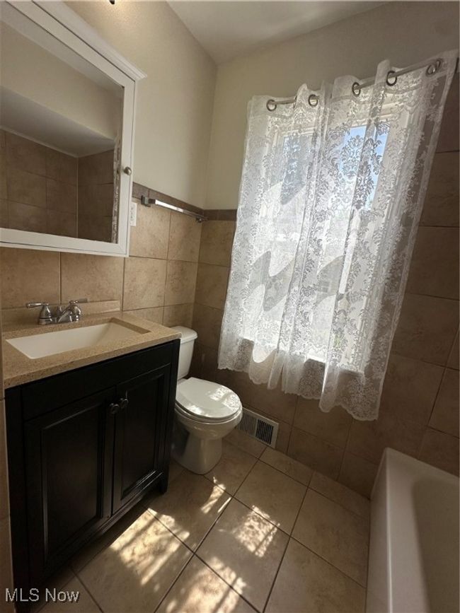 Full bathroom featuring visible vents, toilet, a bath, tile walls, and tile patterned floors | Image 23