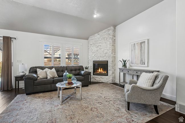 Great room featuring dark wood-type flooring, a stone fireplace, and vaulted ceiling. plantation shutters. | Image 8
