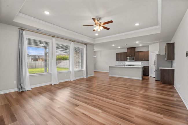 Unfurnished living room featuring a tray ceiling, ornamental molding, a ceiling fan, recessed lighting, and light wood finished floors | Image 4