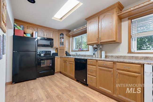 Kitchen with black appliances, light wood finished floors, light countertops, and glass insert cabinets | Image 12