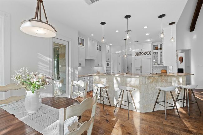 Kitchen featuring glass insert cabinets, a kitchen breakfast bar, light stone counters, dark wood-style flooring, and built in appliances | Image 10