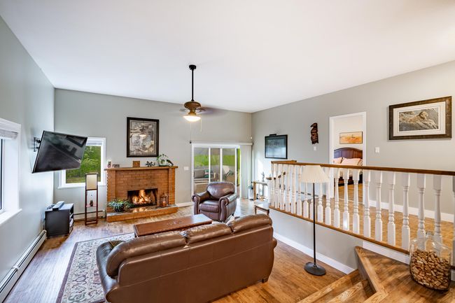 Living area featuring baseboard heating, a ceiling fan, wood finished floors, and a brick fireplace | Image 14