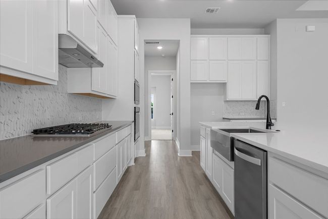 Kitchen with stainless steel appliances, under cabinet range hood, white cabinets, and tasteful backsplash | Image 10