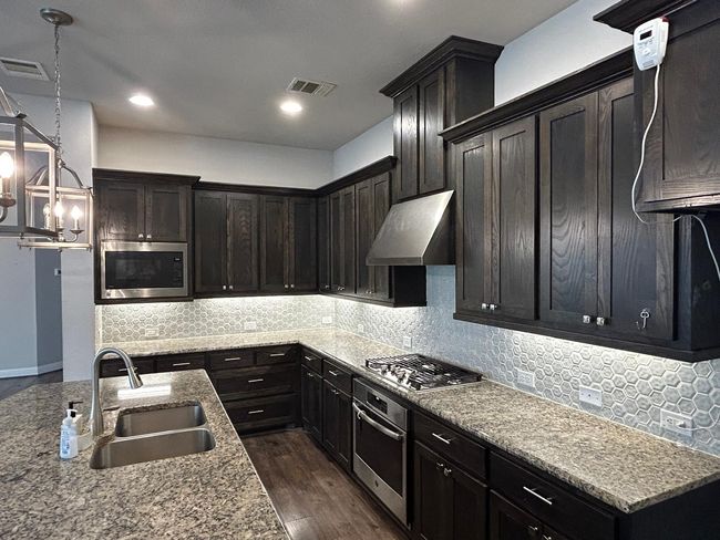 Kitchen featuring appliances with stainless steel finishes, a sink, under cabinet range hood, wood-style flooring, and pendant lighting | Image 13