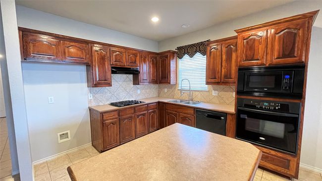Kitchen with black appliances, under cabinet range hood, decorative backsplash, light tile patterned floors, and light countertops | Image 6